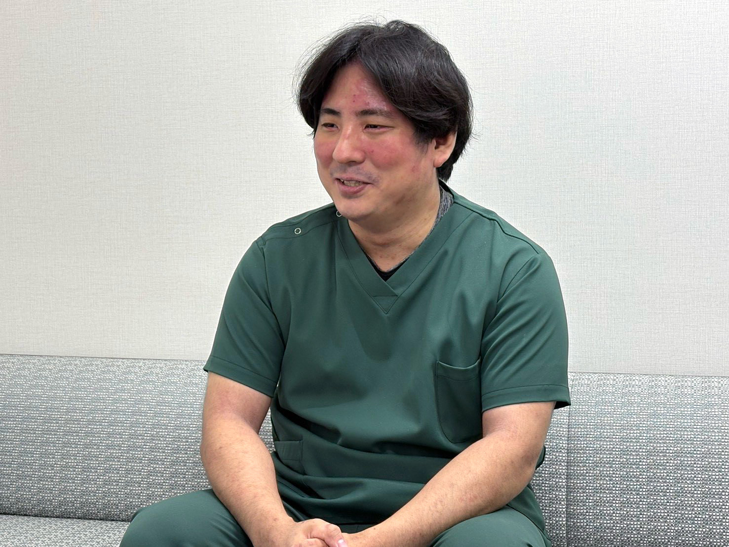 緑色のスクラブ姿でソファに座る山浦義貴医師